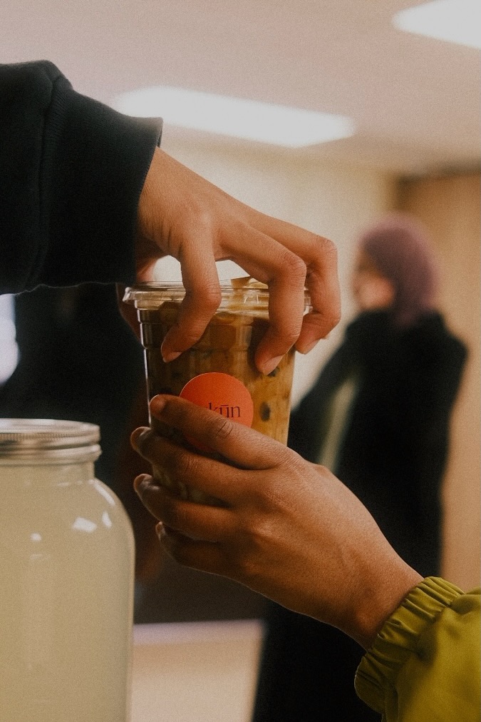 Hands gathered around Sukūn drinks at a community event